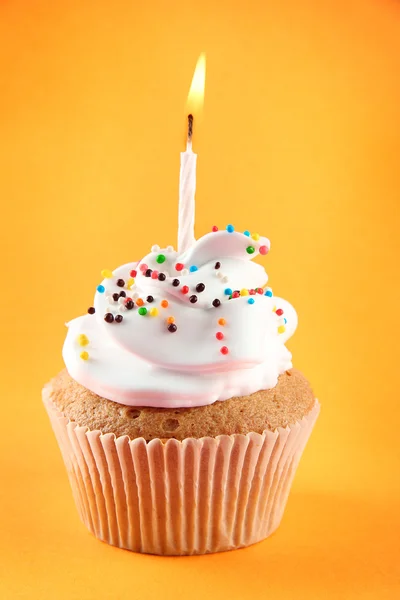 Tasty birthday cupcake with candle, on orange background