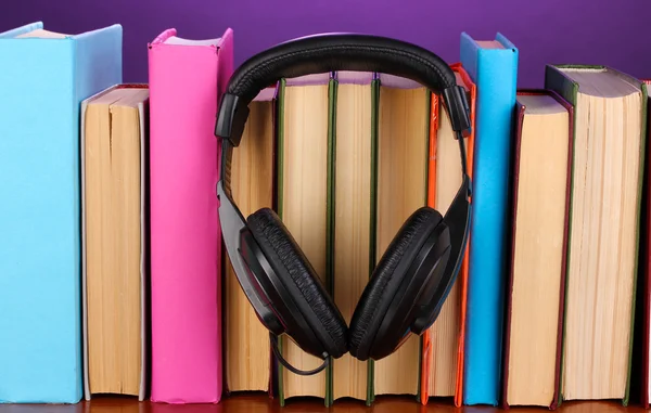 Headphones on books on wooden table on purple background