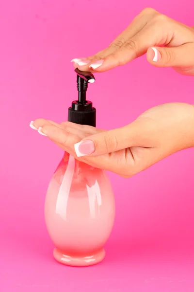 Woman squeezing lotion on her hand, on pink background close-up
