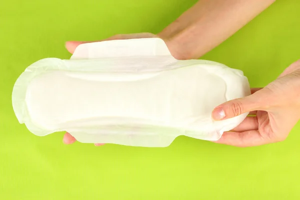 Woman's hands holding a sanitary pad on green background close-up