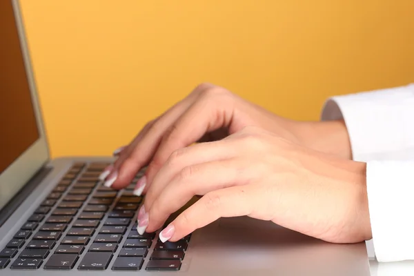 Hands typing on laptop keyboard close up on orange background