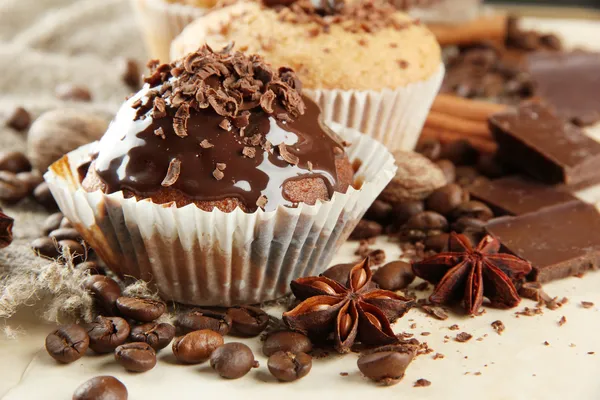 Tasty muffin cakes with chocolate, spices and coffee seeds, on beige backgr