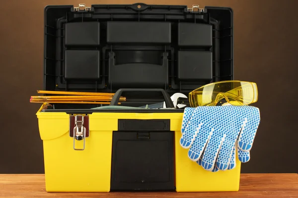 Open yellow tool box with tools on brown background close-up