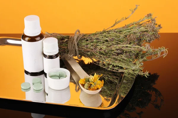 Bottles of medicines and herbs on orange background. concept of homeopathy