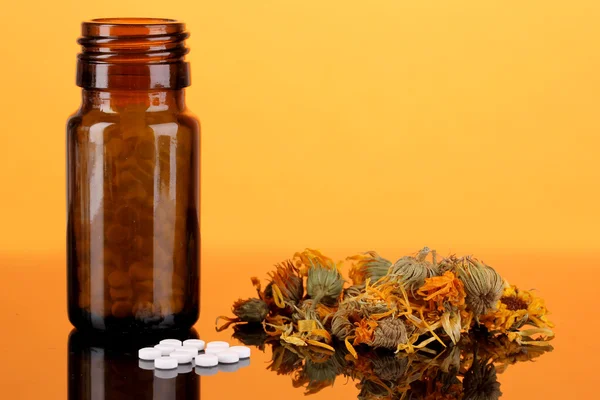 Bottle with pills and herbs on orange background. concept of homeopathy