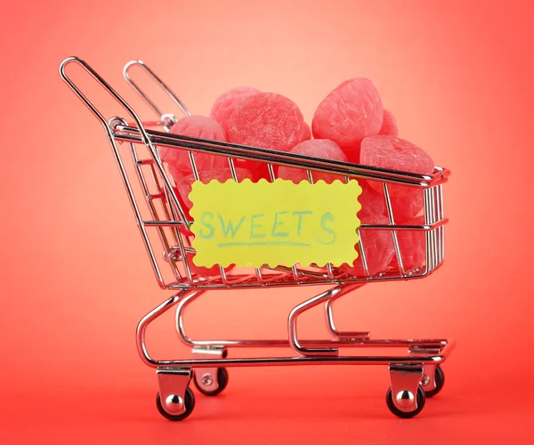 Shopping trolley with jelly candies, on red background — Stock Photo #13745598