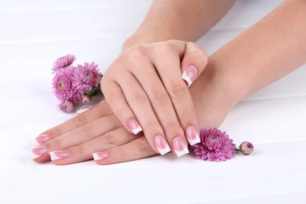 Woman hands with french manicure and flowers on white wooden background