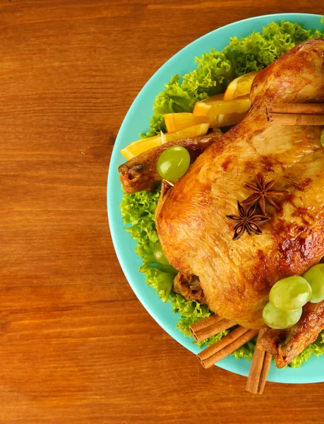 Whole roasted chicken with lettuce, grapes, oranges and spices on blue plat