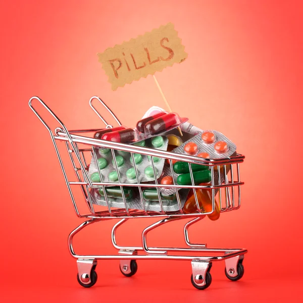 Shopping trolley with pills, on red background