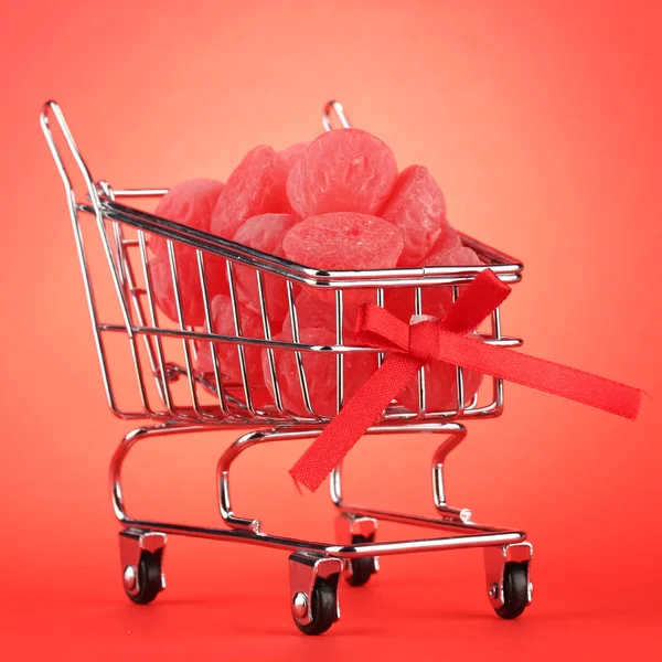 Shopping trolley with jelly candies, on red background — Stock Photo #13870868