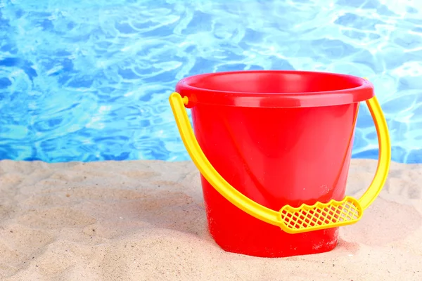 Children's bucket on sand on water background