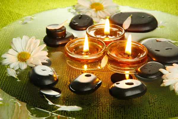 Spa stones with flowers and candles in water on plate