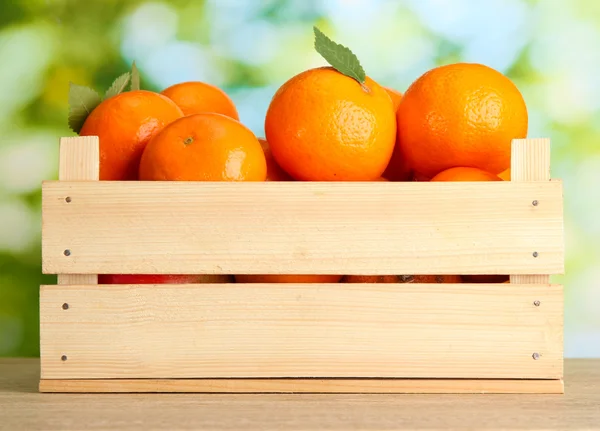 Ripe tasty tangerines with leaves in wooden box on table on green backgroun