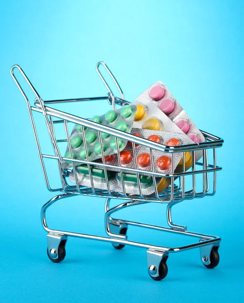 Shopping trolley with pills, on blue background