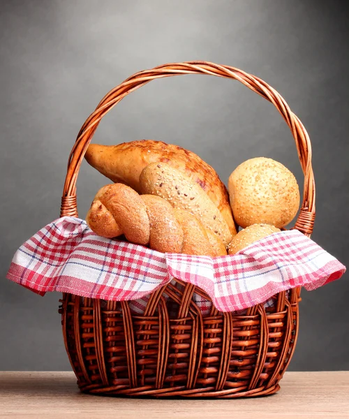 Delicious bread in basket on wooden table on gray background