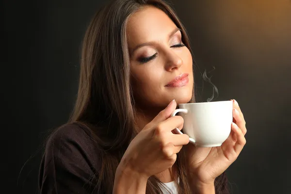 Beautiful young woman with cup of coffee on brown background
