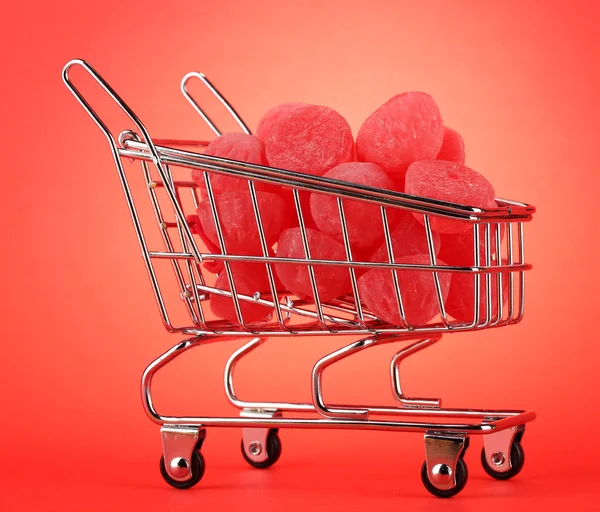 Shopping trolley with jelly candies, on red background