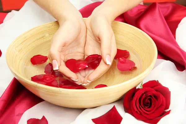 Woman hands with wooden bowl of water with petals, on red background