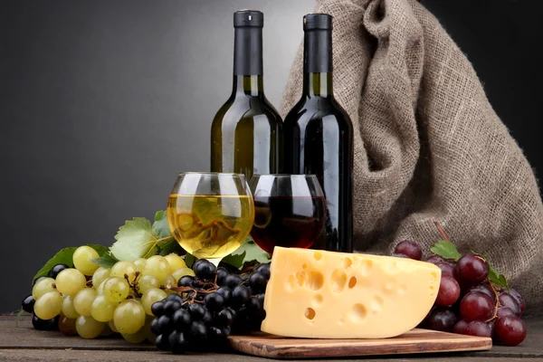 Bottles and glasses of wine, cheese and grapes on grey background