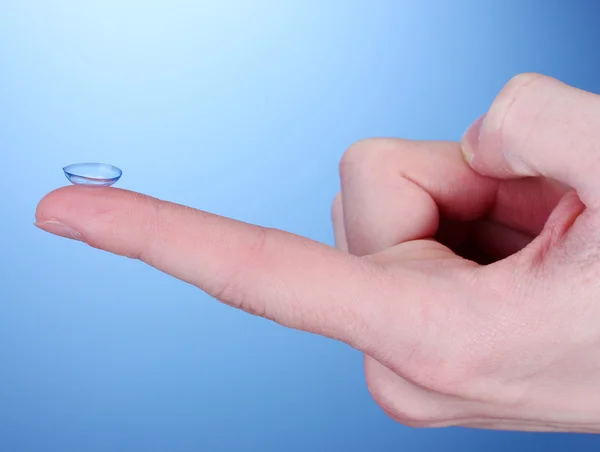 Contact lens on finger on blue background