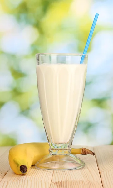 Banana milk shake on wooden table on bright background