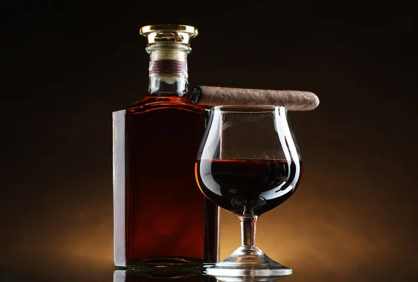 Bottle and glass of brandy and cigar on brown background