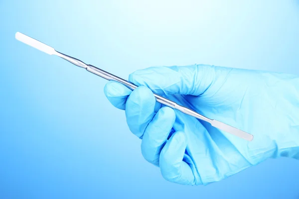 Hand in blue glove holding dental tool on blue background