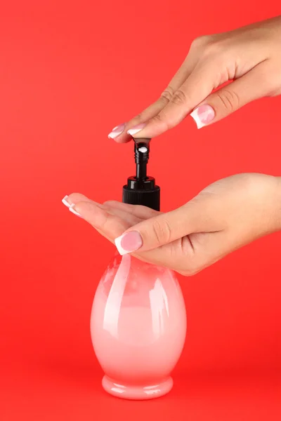 Woman squeezing lotion on her hand, on red background close-up