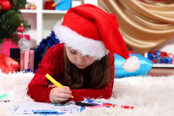 Beautiful little girl writes letter to Santa Claus in festively decorated room