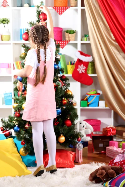 Little girl decorates Christmas tree in festively decorated room