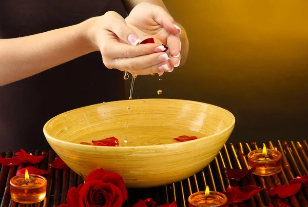 Woman hands with wooden bowl of water with petals, on brown background