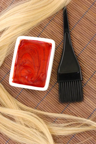 Hair dye in bowl and brush for hair coloring on brown bamboo mat, close-up
