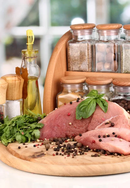 A large piece of pork marinated with herbs, spices and cooking oil on board on white table on window background