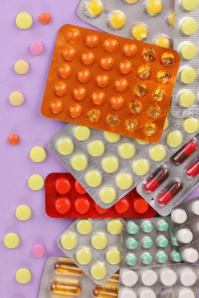 Capsules and pills packed in blisters on purple background