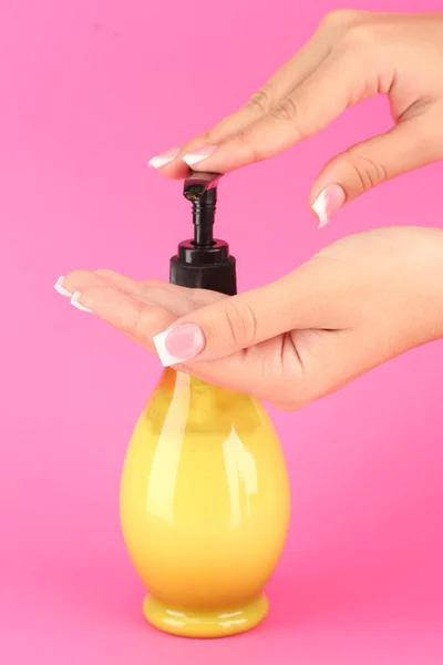 Woman squeezing lotion on her hand, on pink background close-up