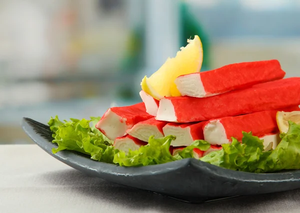 Crab sticks with lettuce leaves and lemon on plate, close up