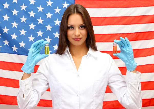 Portrait of female doctor or scientist showing and analyzing liquid in flask over American Flag background