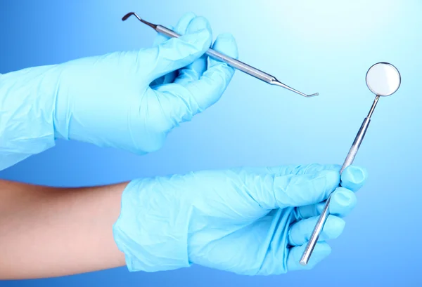 Hands in blue gloves holding dental tools on blue background