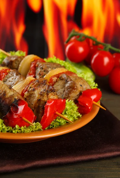 Tasty grilled meat and vegetables on plate, on fire background