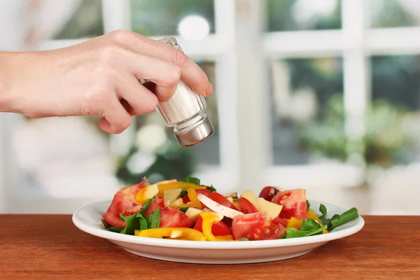 Hand adding salt using salt shaker on bright background