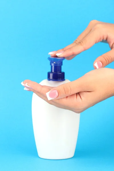 Woman squeezing lotion on her hand, on blue background close-up