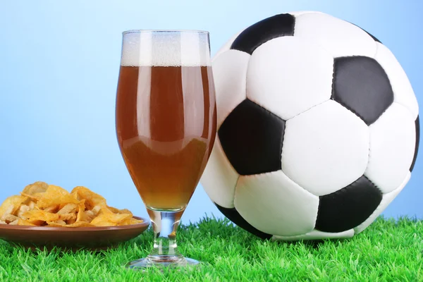 Glass of beer with soccer ball on grass on blue background