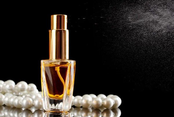 Women\'s perfume in beautiful bottle and beads, on black background
