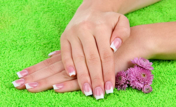 Woman hands with french manicure and flowers on green towel