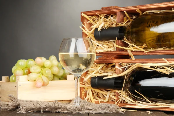 Wooden case with wine bottles, wineglass and grape on wooden table on grey background