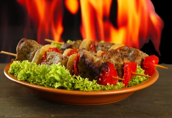 Tasty grilled meat and vegetables on plate, on fire background