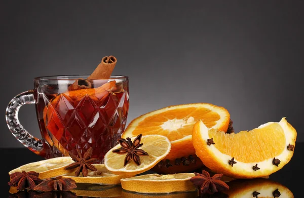 Fragrant mulled wine in glass with spices and oranges around on black background