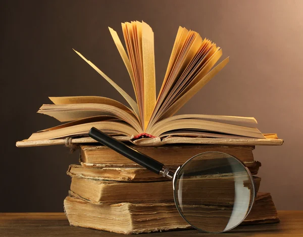Magnifying glass and books on table on brown background