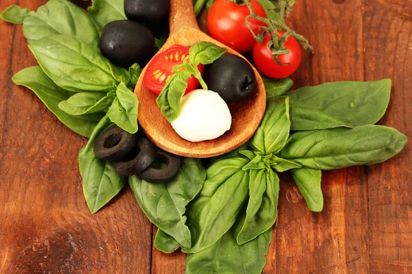 Cheese mozzarella with vegetables in wooden spoon on wooden background close-up