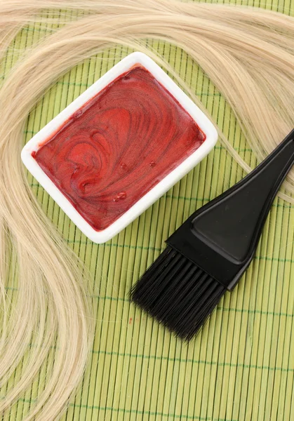 Hair dye in bowl and brush for hair coloring on green bamboo mat, close-up